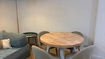 Una sala de estar moderna con una mesa redonda de madera, sillas tapizadas en gris, un sofá gris con cojines, un tapete tejido y una lámpara colgante.