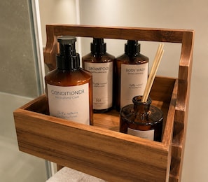 A wooden tray holding three bottles of personal care products, including conditioner, shampoo, and body wash. - Luxury Marylebone Penthouse (London)