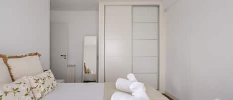 A bedroom with a bed, a bedside table, a mirror, and a towel on the floor.