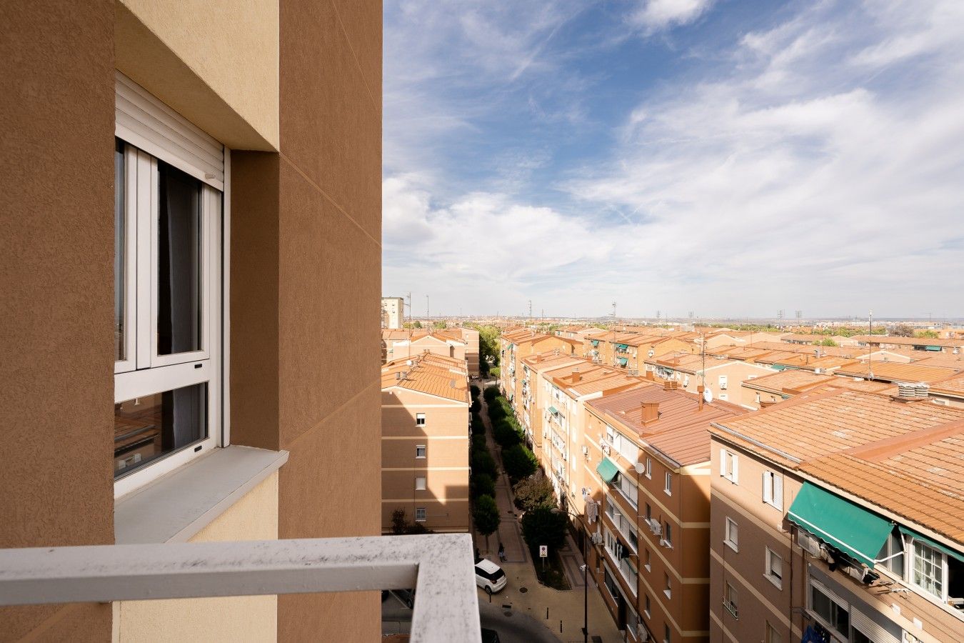 Un balcón con vista a una zona residencial, con varios edificios de techos planos y cielo despejado.