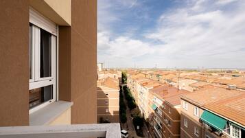 Un balcon donnant sur un quartier résidentiel, avec plusieurs immeubles dotés de toits plats et un ciel dégagé.