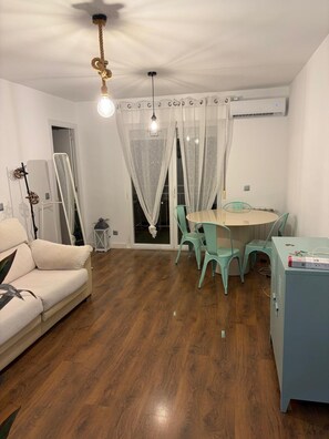 Una habitació amb un sofà, una taula de dinar amb cadires, un llum al sostre i un radiador.
