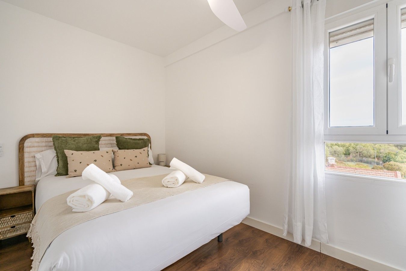 Un dormitorio con cama, almohadas, mesita de noche y ventana con cortinas.