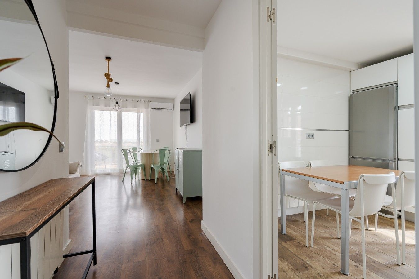 Una cocina moderna con armarios blancos, un refrigerador de acero inoxidable y una mesa de comedor de madera con sillas.