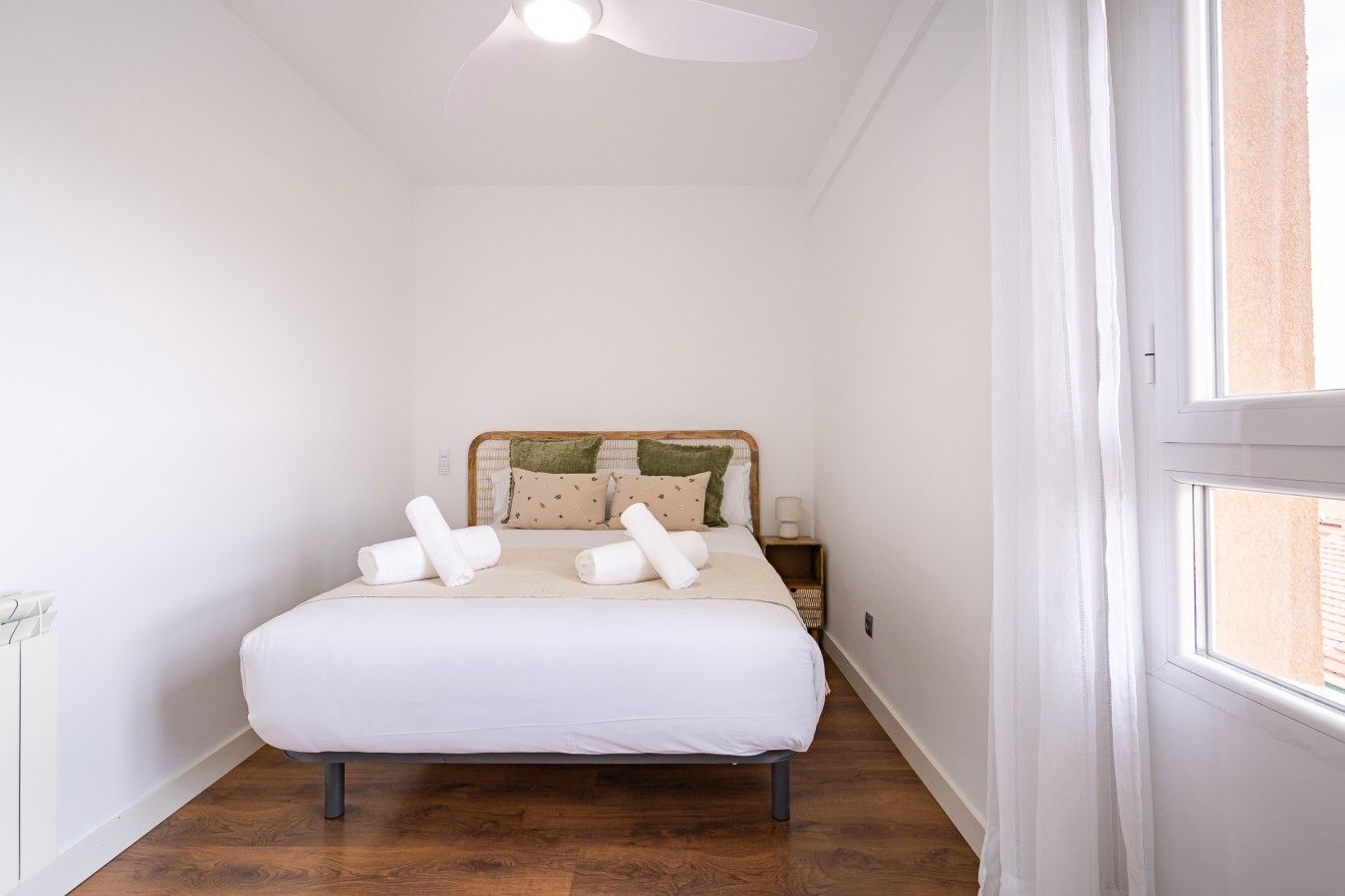 A bedroom with a bed, pillows, a nightstand, a ceiling fan, and a window.