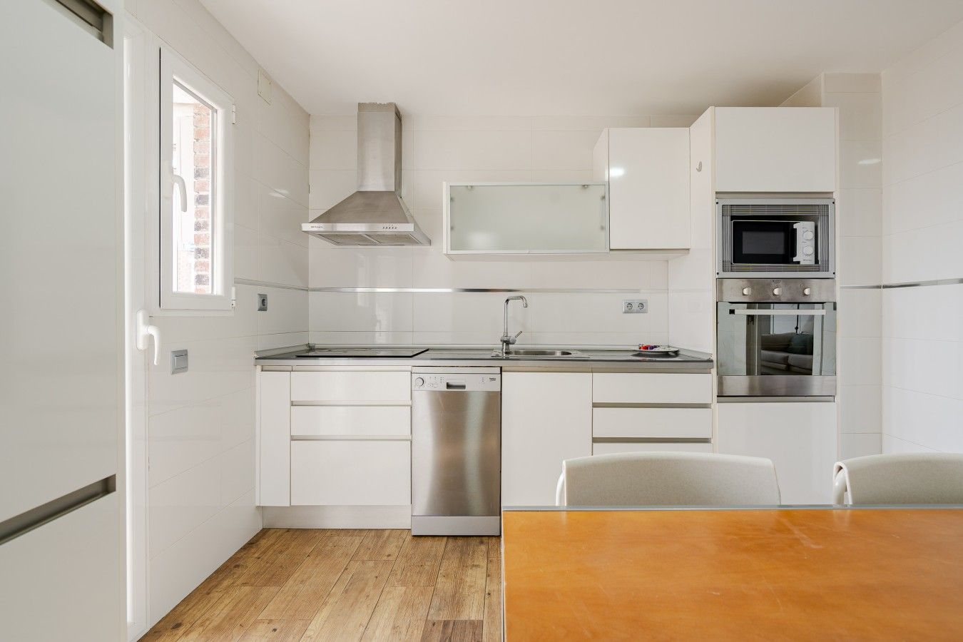 Una cocina moderna con armarios blancos, lavavajillas de acero inoxidable, microondas y horno.