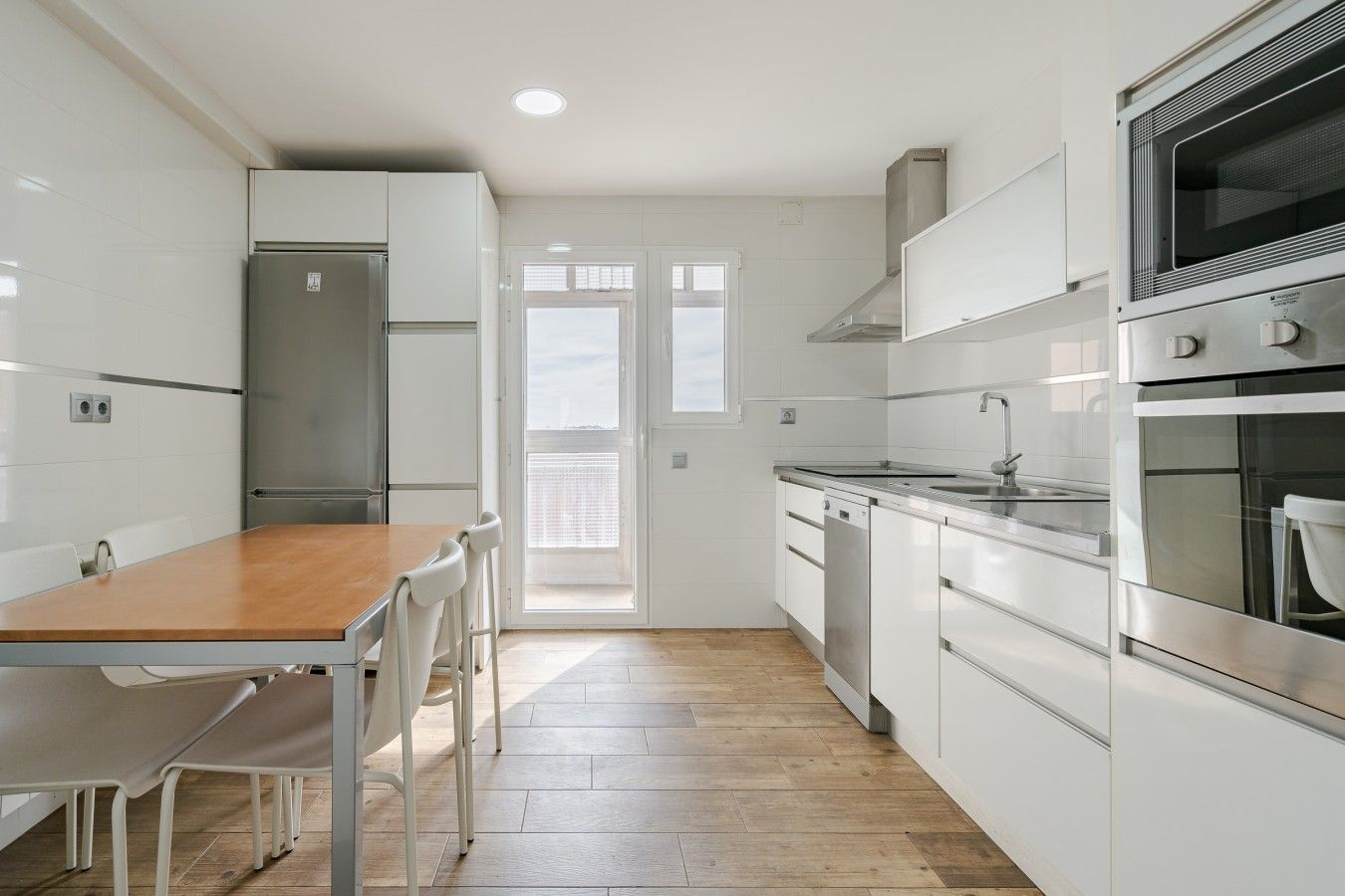 A modern kitchen with white cabinets, stainless steel appliances, and a wooden dining table.