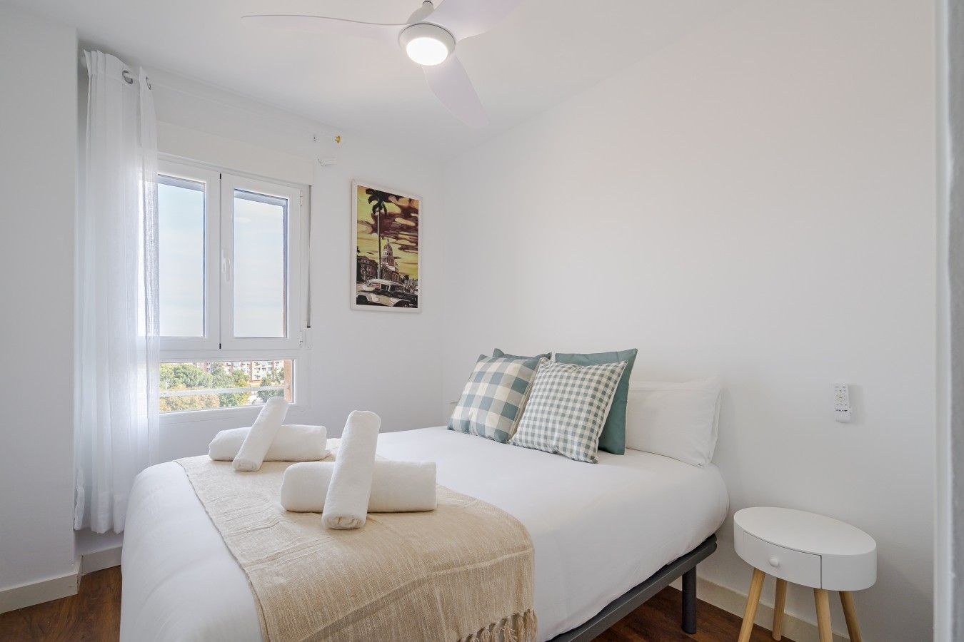 Un dormitorio con cama, mesita de noche, ventana con cortinas y lámpara de pared.