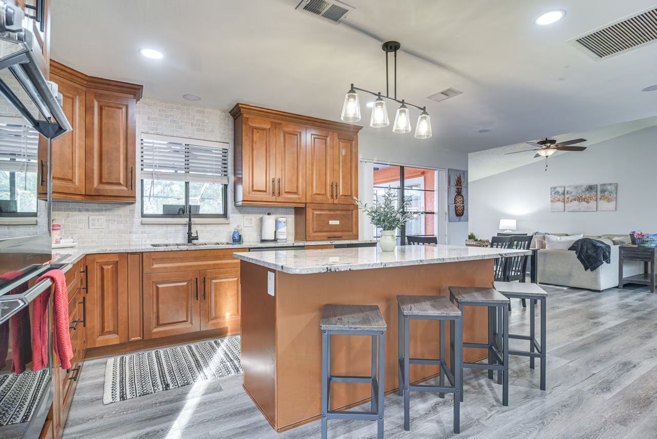 A modern kitchen with wooden cabinets, a large island with stools, and pendant lighting.