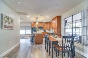 A modern kitchen with wooden cabinets, a central island, and a dining area with chairs. - Largo Oasis w/ Pool & Grill~6 Mi to Beach! (Largo)