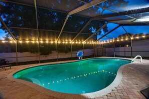 A swimming pool with a basketball hoop, surrounded by a covered area with string lights. - Largo Oasis w/ Pool & Grill~6 Mi to Beach! (Largo)