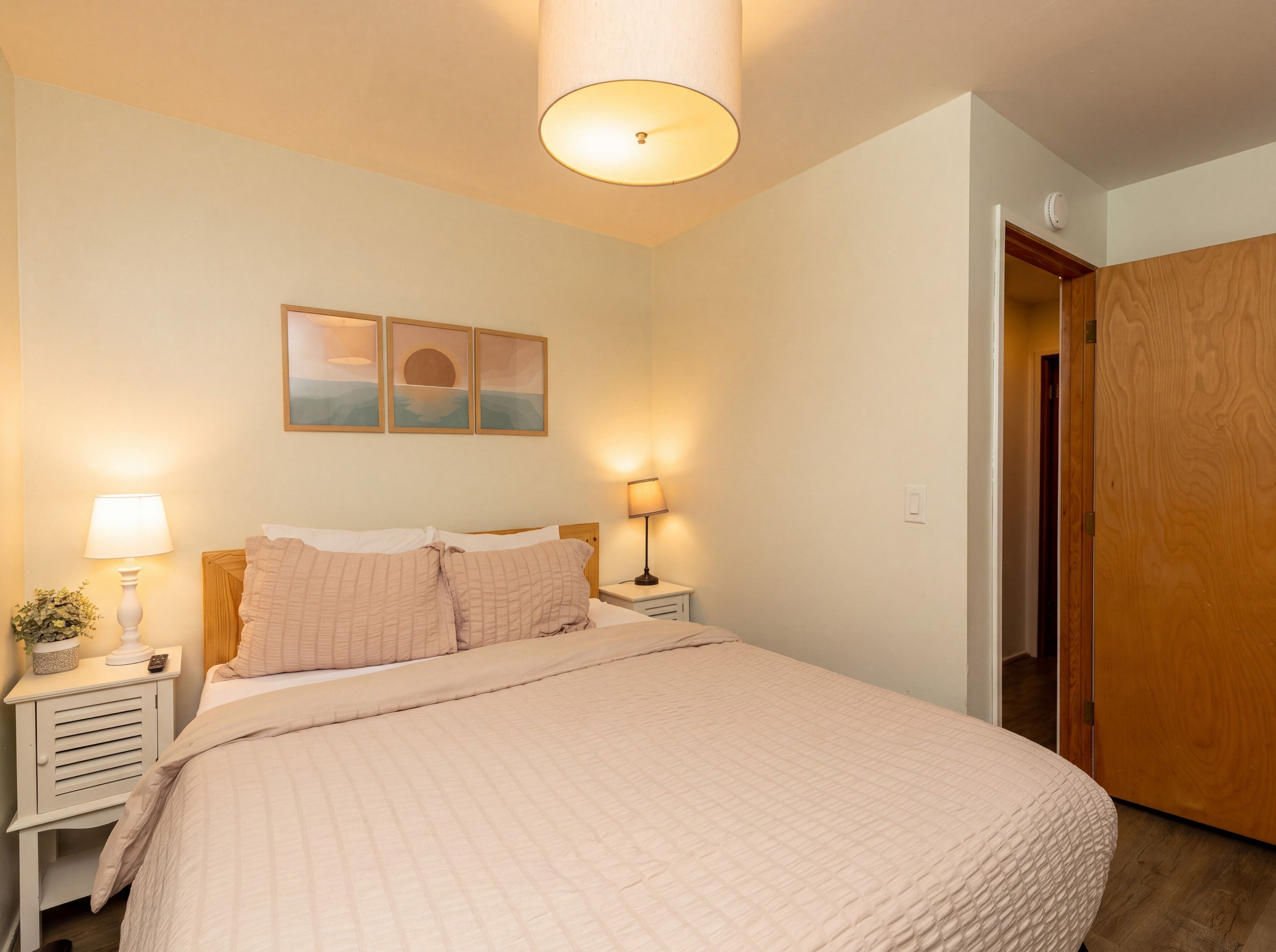 A bedroom with a bed, bedside lamps, a nightstand, a wall-mounted lamp, and a door.