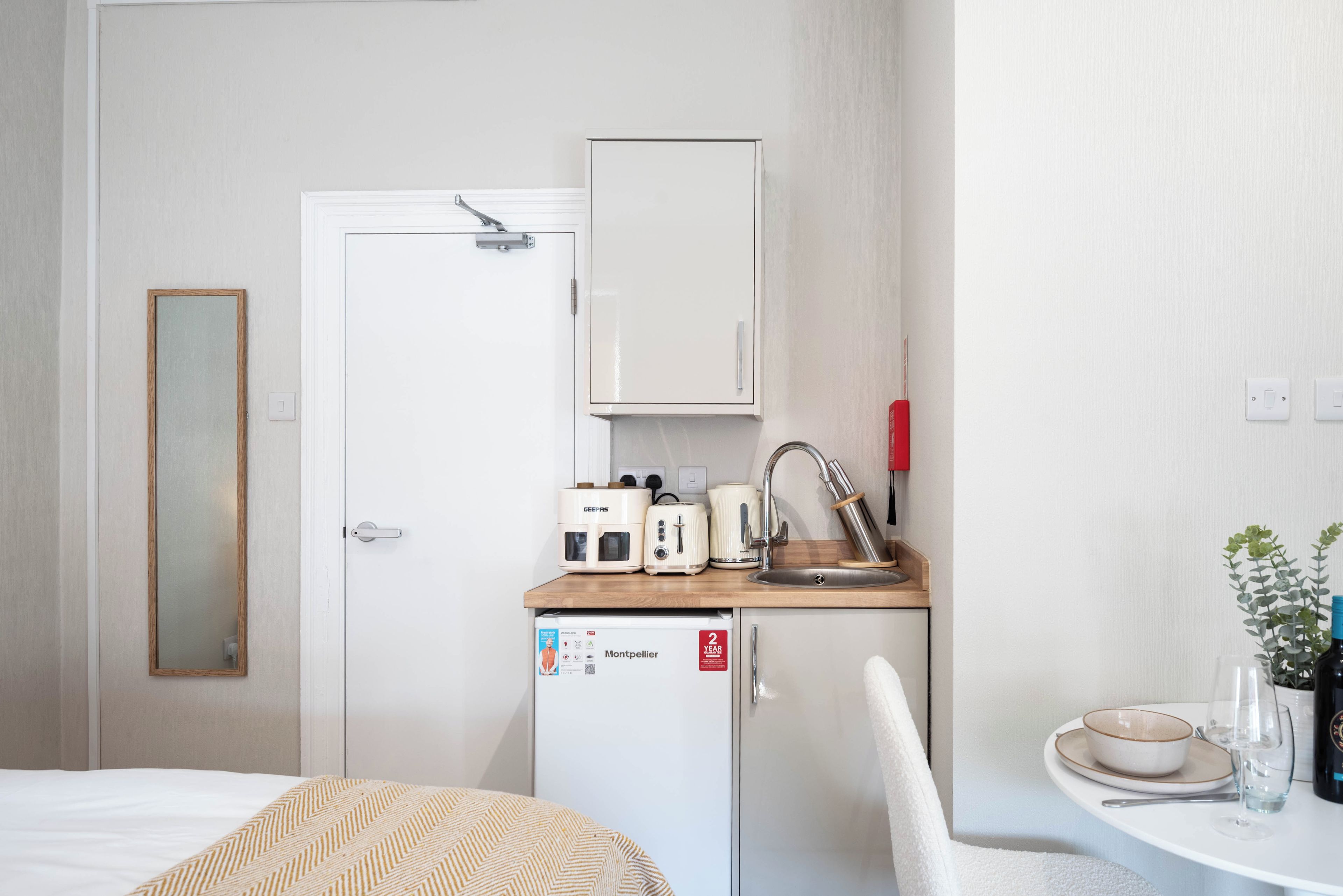 Habitación de hotel compacta con una cama, una kitchenette pequeña con refrigerador, un lavamanos y un espejo.