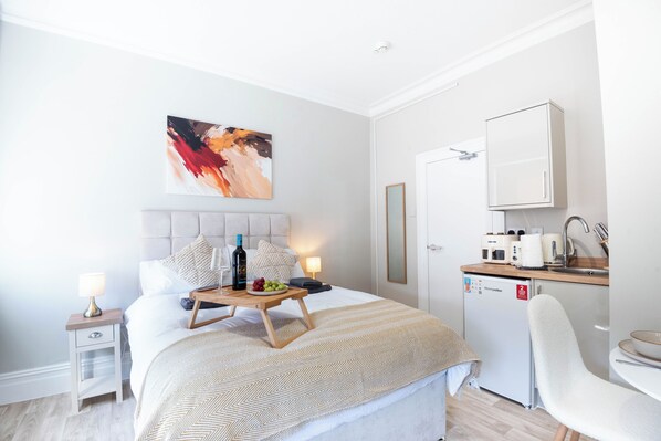 Une chambre d’hôtel comprenant un lit, une table de chevet, une lampe, des œuvres d’art, ainsi qu’une kitchenette équipée d’un réfrigérateur, d’un four à micro-ondes et d’une machine à café.