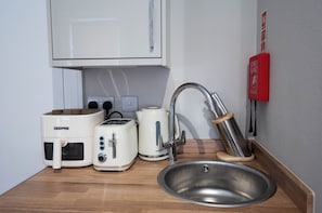 Ett litet kök med en mikrovågsugn från GEEPAS, en brödrost från Breville, en vattenkokare från Breville och en diskho i rostfritt stål.