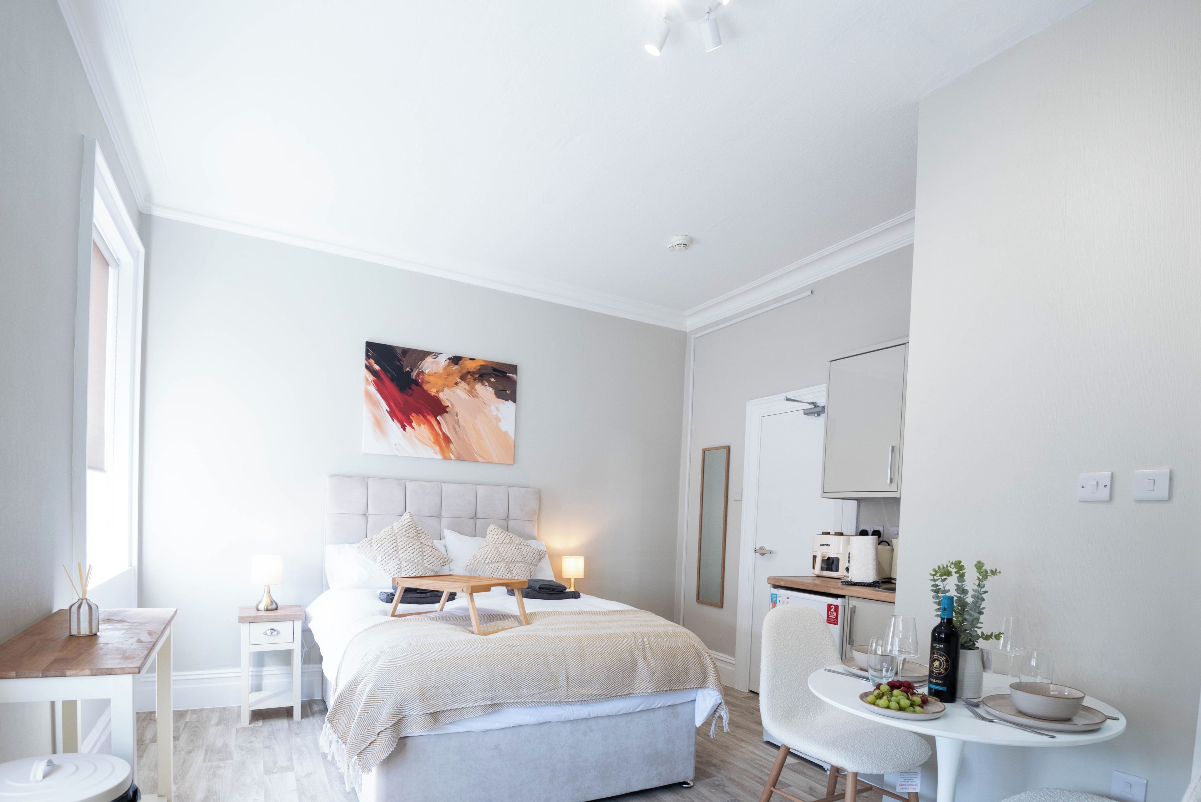 A modern bedroom with a bed, bedside tables, a desk, a chair, a mirror, and a wall-mounted artwork.