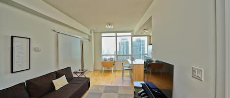 Un salon moderne avec un canapé, une table basse, un piano et une vue sur la ville grâce à de grandes fenêtres.