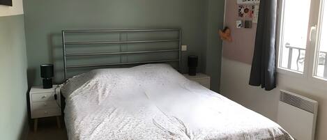 Une chambre à coucher avec un lit, des tables de chevet, une étagère fixée au mur et une fenêtre avec des rideaux.
