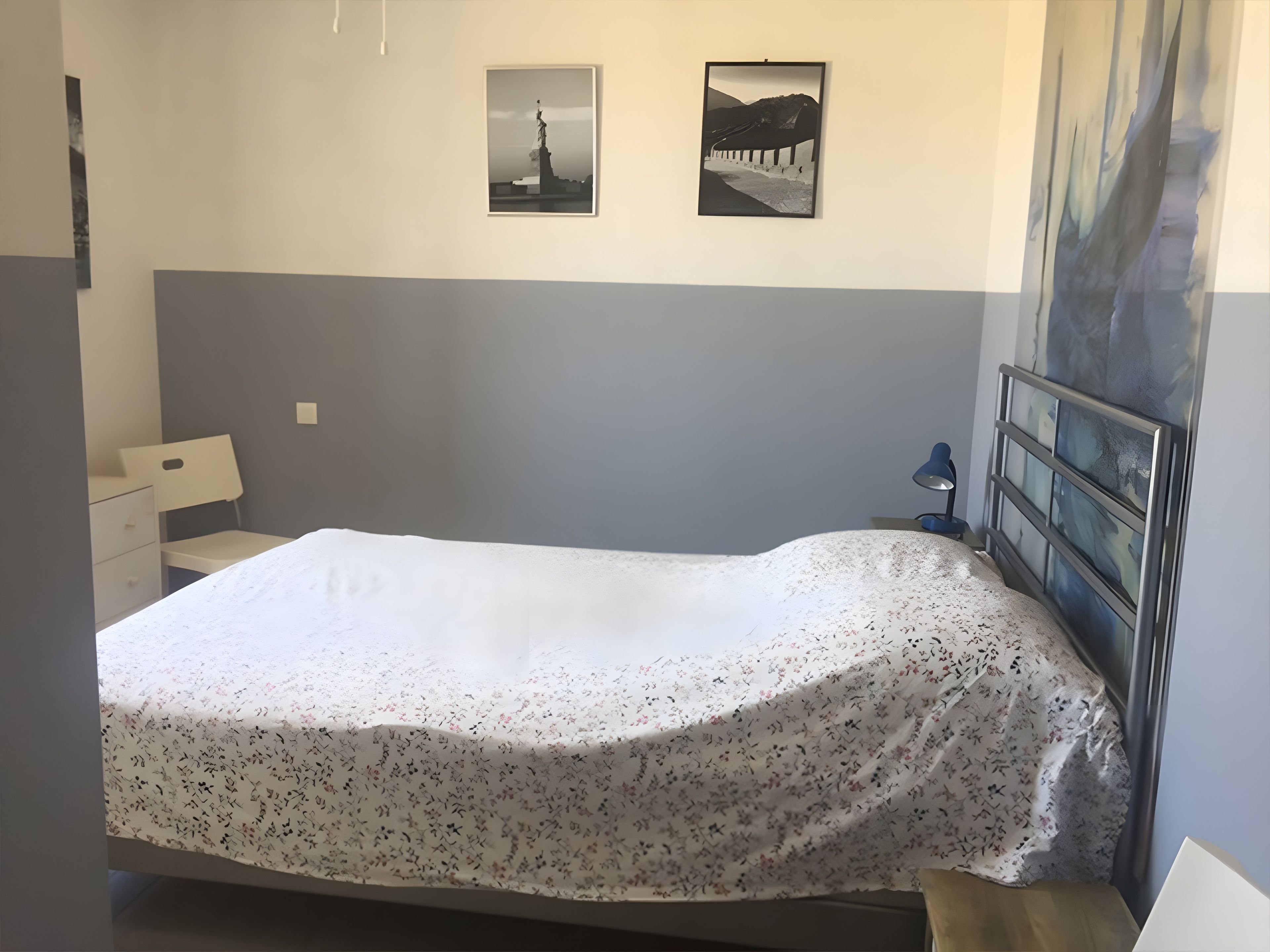 A bedroom with a bed, a nightstand, a desk, and two framed pictures on the wall.