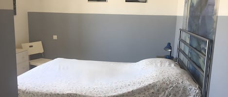A bedroom with a bed, a nightstand, a desk, and two framed pictures on the wall.