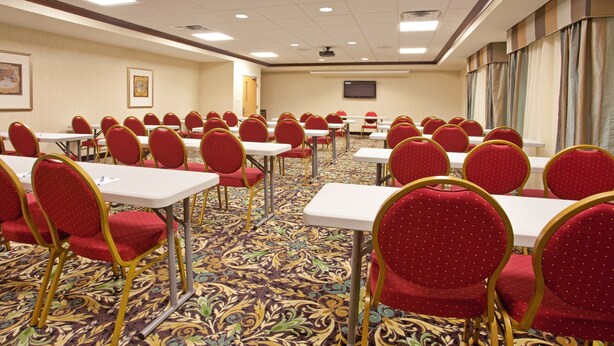 A conference room with rows of tables and chairs, carpeted floor, and a projector screen on the wall. - Accessible Suite w/ Kitchen | Free Breakfast! (Elkhart)