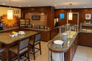 A hotel breakfast area with a stone wall, a sign for free daily breakfast, and a buffet counter with various food items.