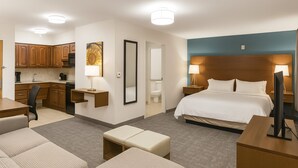 Una habitación de hotel con cama, mesitas de noche, escritorio, silla, sofá, una pequeña mesa y kitchenette.