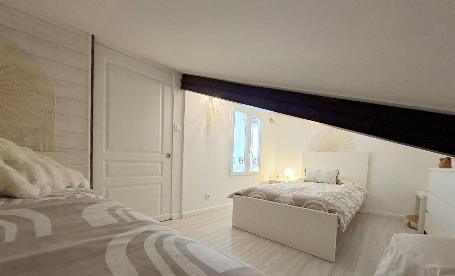A bedroom with a large bed, a smaller bed, a wardrobe, a nightstand, and a window with a view.