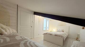 A bedroom with a large bed, a smaller bed, a wardrobe, a nightstand, and a window with a view.