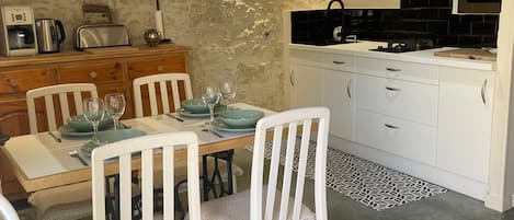Una cocina moderna con armarios blancos, una mesa de comedor para cuatro personas y lámparas colgantes.