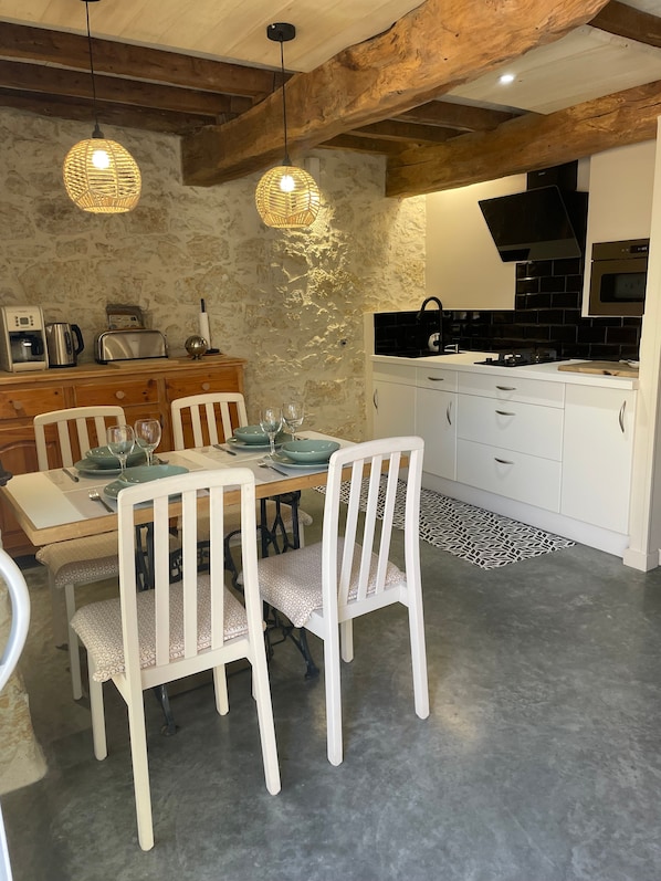 Une cuisine moderne avec des meubles blancs, une table à manger pour quatre personnes et des luminaires suspendus.
