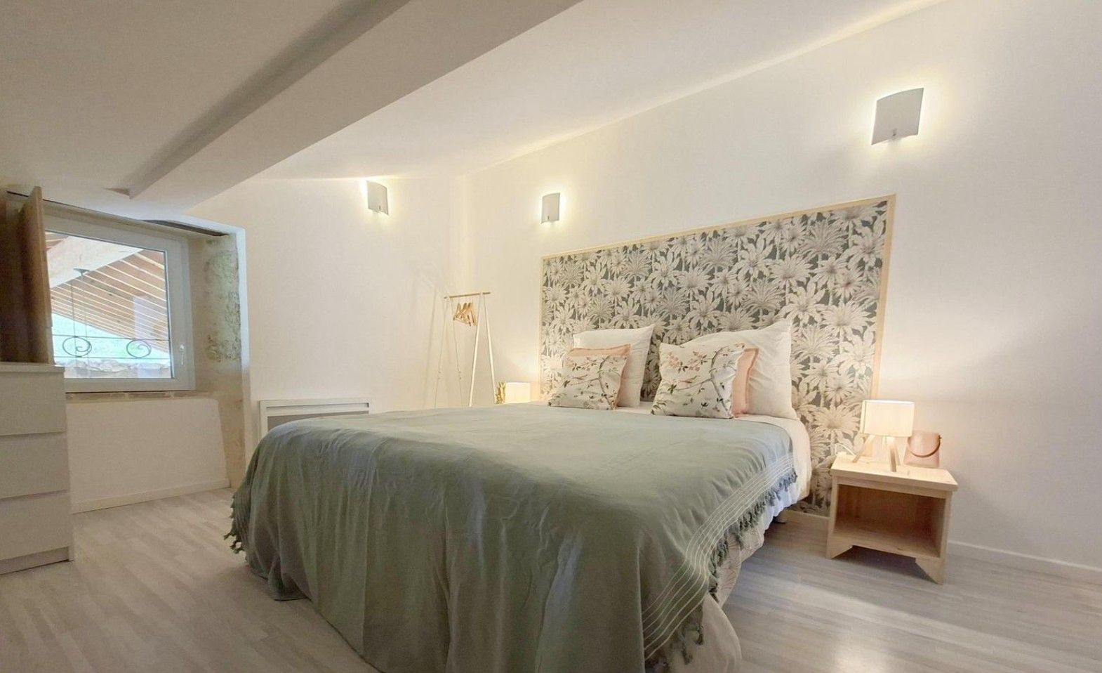 A bedroom with a bed, bedside tables, a window, and a wall with a floral pattern.