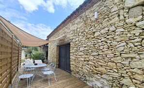 Un mur en pierre avec une terrasse en bois et des chaises en métal.