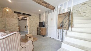 Et værelse med en stenvæg, en trætrappe, et fjernsyn på et skab og en stribet sofa.
