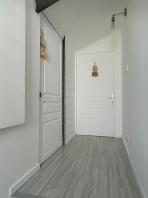 Un couloir avec une porte blanche, un luminaire et une décoration suspendue.