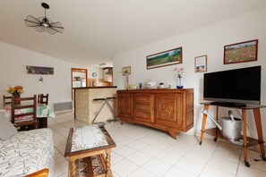 Un salon comprenant un canapé, un meuble en bois, un téléviseur et un coin repas avec des chaises et une table.