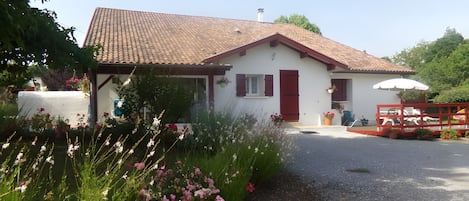 Une maison à deux étages, avec un toit recouvert de tuiles rouges, une façade blanche et une porte rouge.