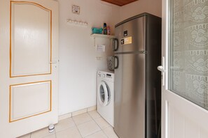 A compact kitchen with a stainless steel refrigerator, a washing machine, and a door with a simple design. - Gîte Chez Françoise et Jean: natural air conditioning in Saint-Lon-les-Mines (Saint-Lon-les-Mines)