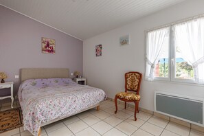 Une chambre à coucher avec un lit, une chaise, une fenêtre avec des rideaux et un radiateur.