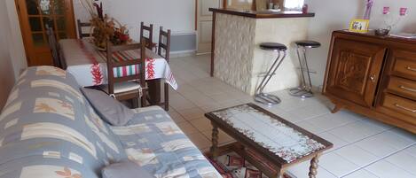 Un salon avec un canapé, une table à manger avec des chaises, un coin cuisine et un tabouret de bar.