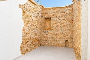Un patio de muros de piedra con suelo de baldosas, una ventana pequeña y luces colgantes.
