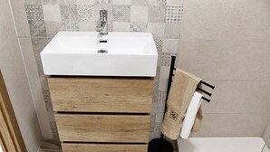 Casa de banho com lavatório branco, gavetas de madeira, esgoto preto no chão e azulejos estampados na parede.