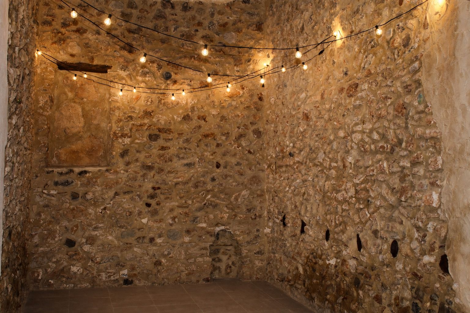 A stone-walled room with string lights, a bed, and a small window.