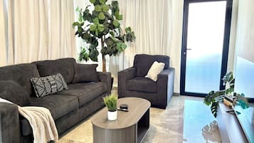 Een moderne woonkamer met een grijze bank, een bijpassende fauteuil, een salontafel en een grote plant.