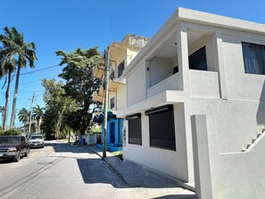 Un edificio moderno de dos pisos con fachada blanca, una puerta azul y una escalera visible.