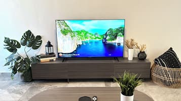A flat-screen TV on a dark wooden TV stand, with a remote control and a potted plant on a round wooden coffee table.