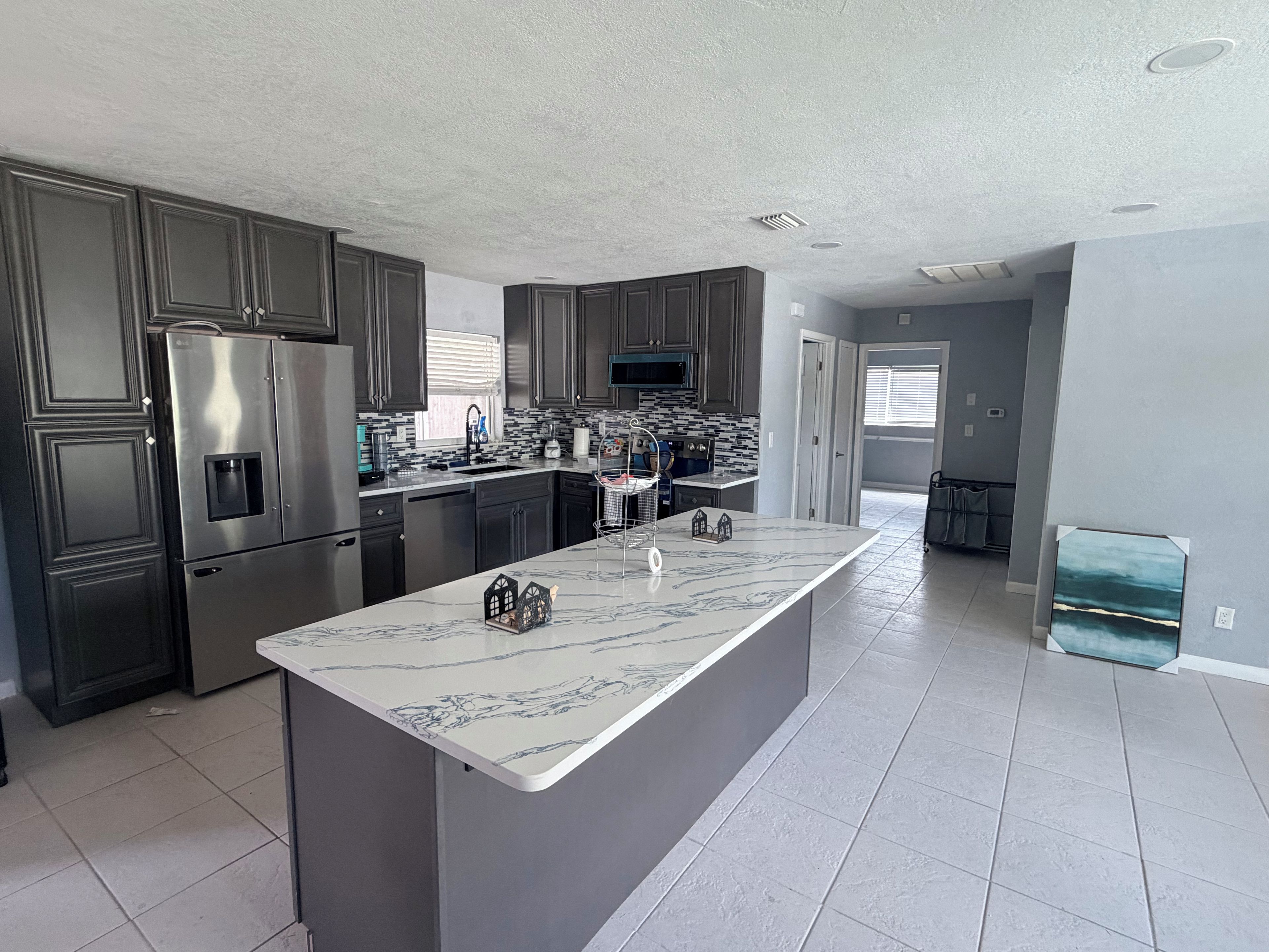 A modern kitchen with dark cabinetry, stainless steel appliances, and a marble island.