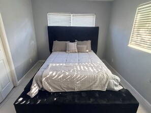 Ein Schlafzimmer mit einem Bett, einem Kopfteil und einem Fenster mit Jalousien.