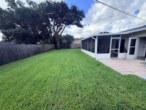Ein Garten mit gepflegtem Rasen, Holzzaun und überdachter Terrasse.