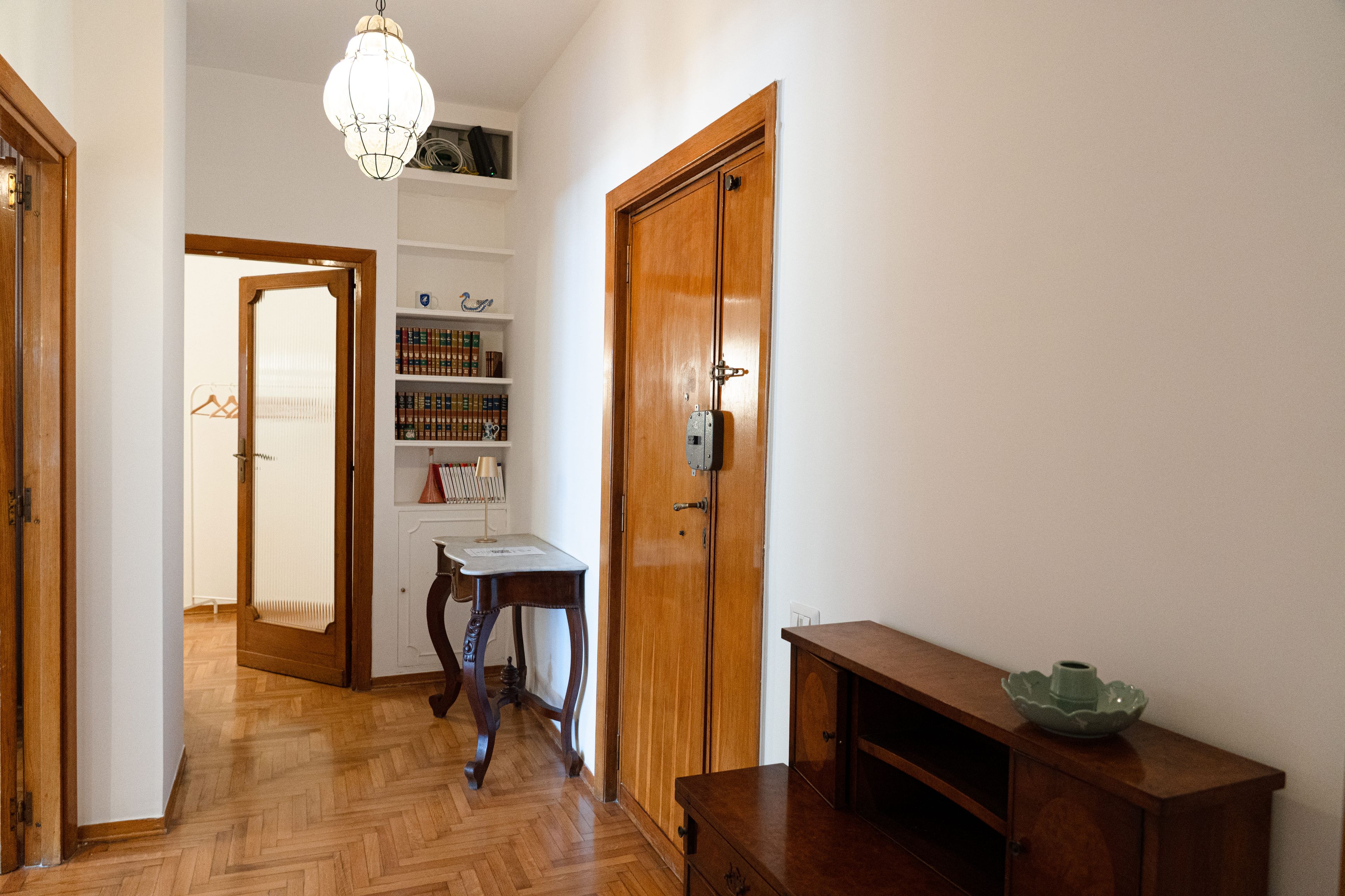 A hallway with wooden flooring, a wooden door, a desk, and a bookshelf.